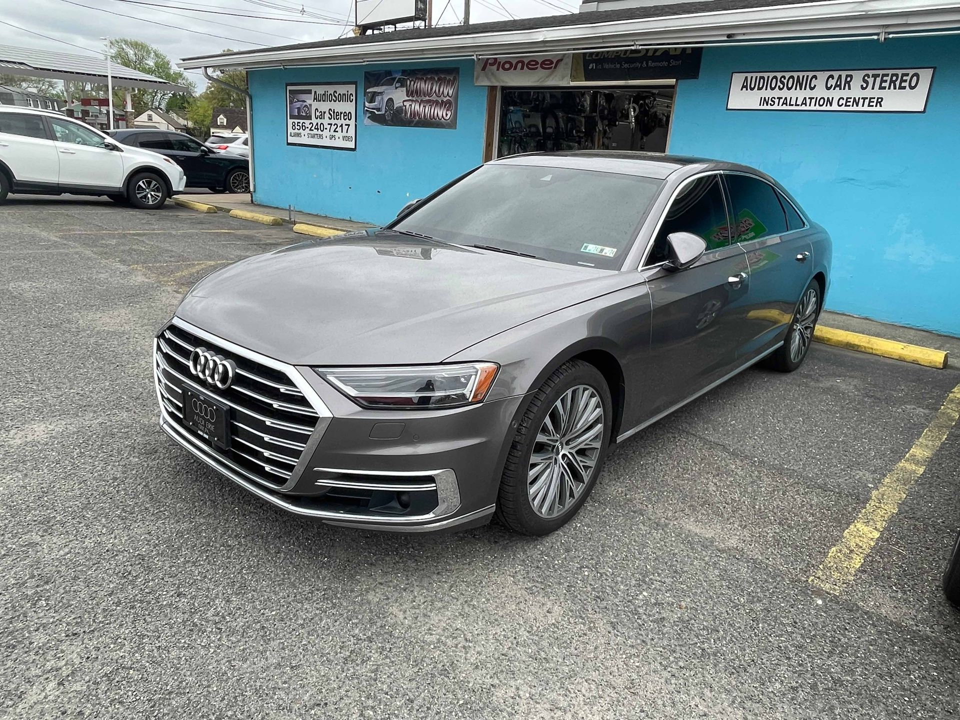 A gray audi a8 is parked in a parking lot in front of a blue building.
