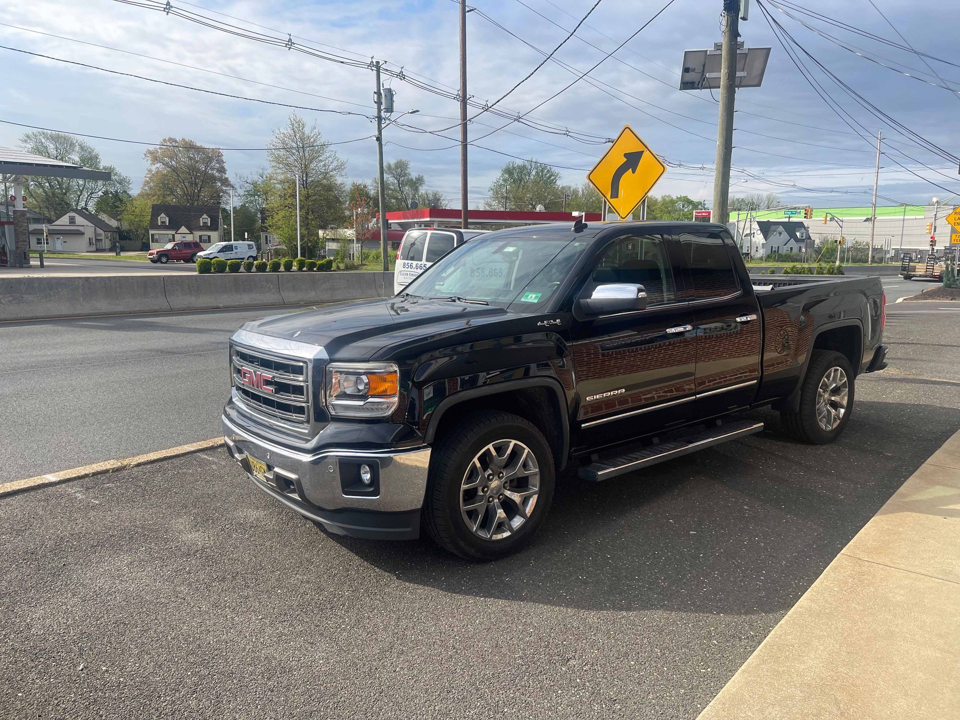 A black pickup truck is parked on the side of the road next to a yellow sign.