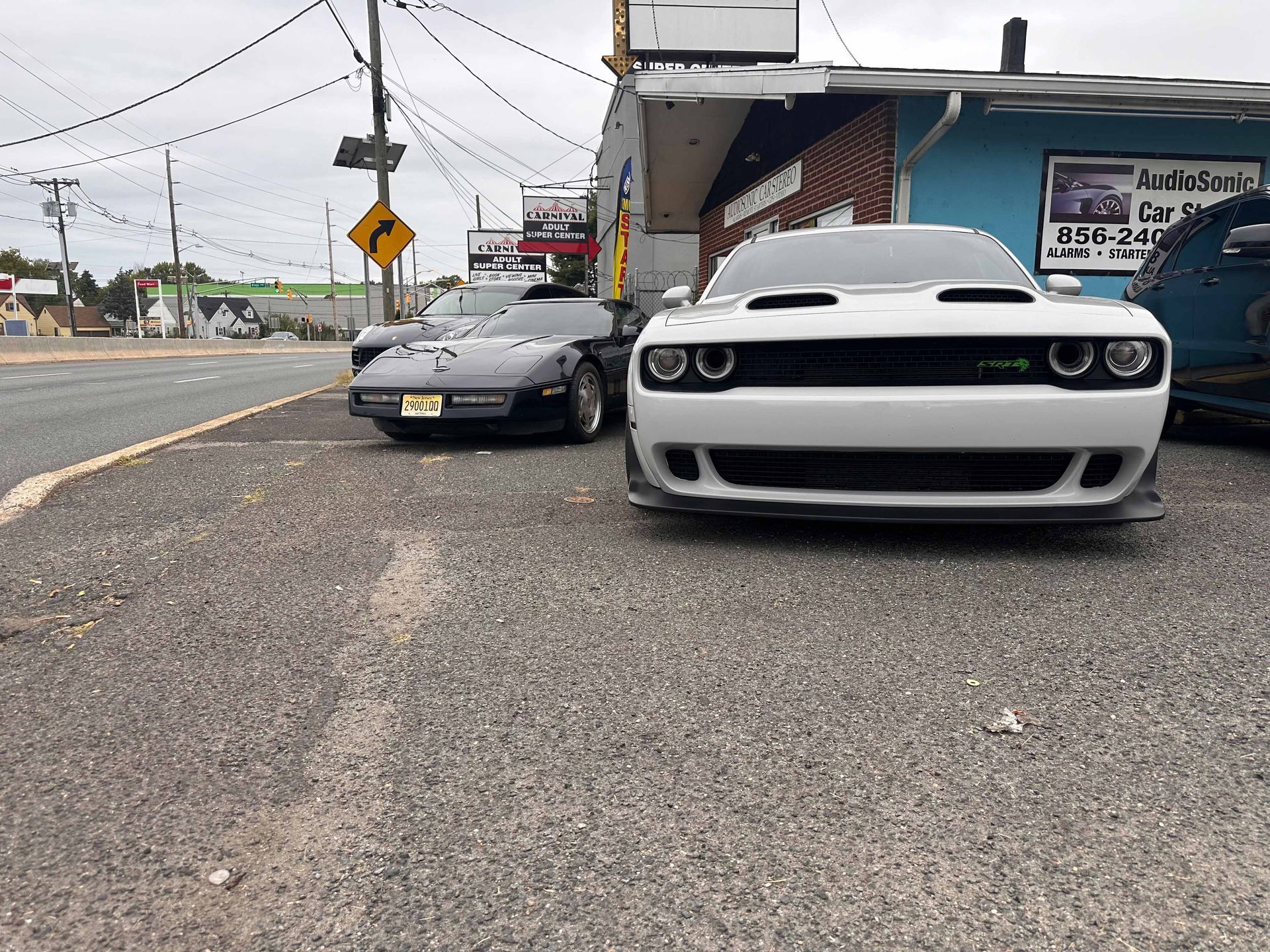 A white dodge challenger is parked in a parking lot next to a corvette.