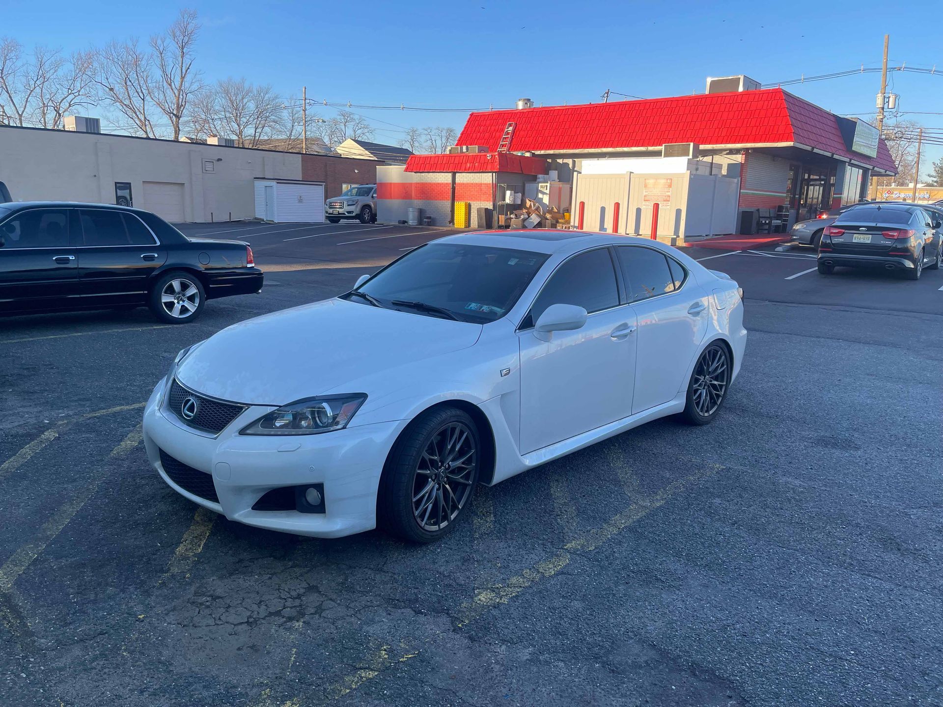 A white car is parked in a parking lot in front of a red building.
