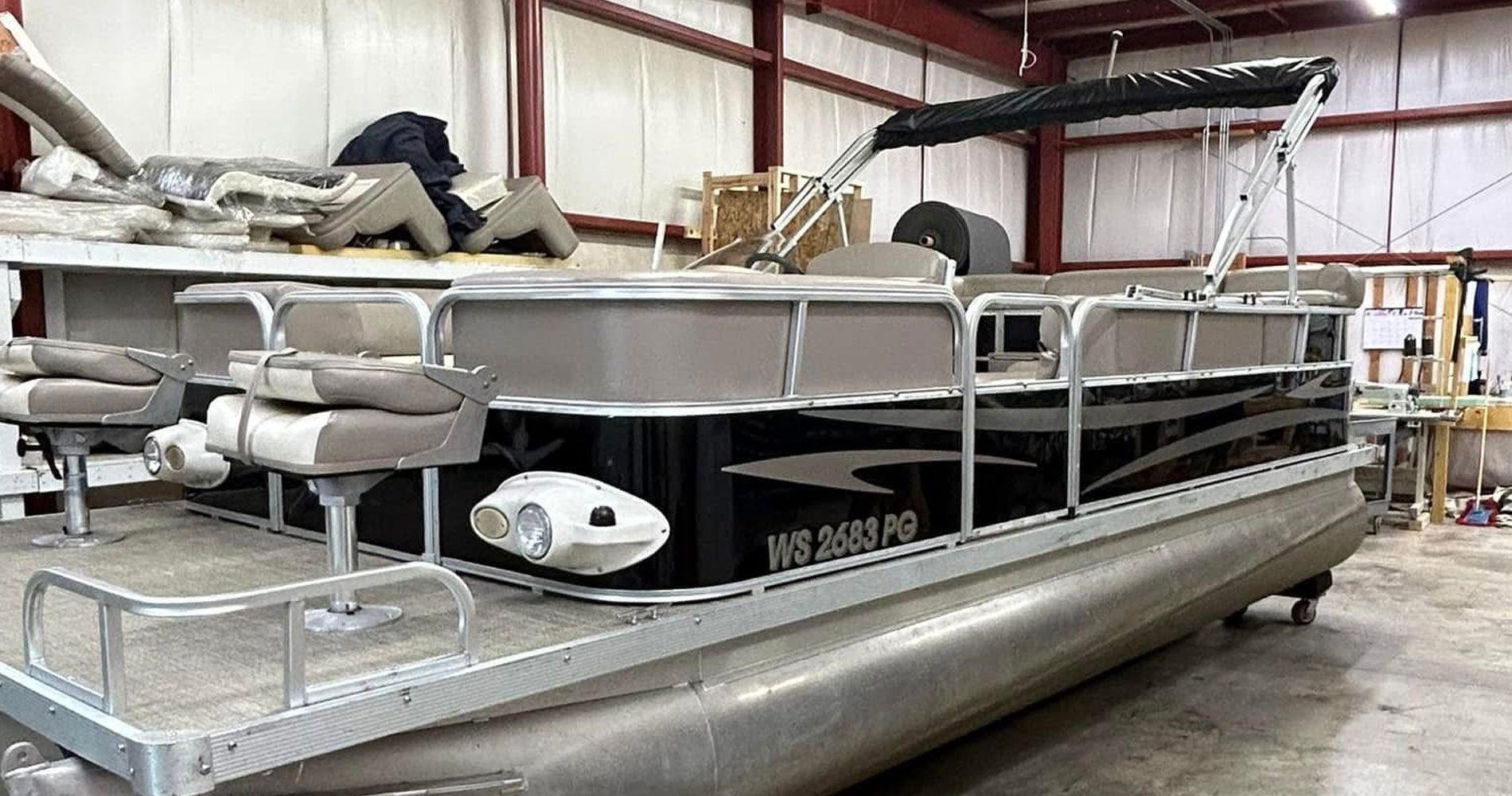 Pontoon boat in a warehouse with aluminum railings and beige seats on a trailer