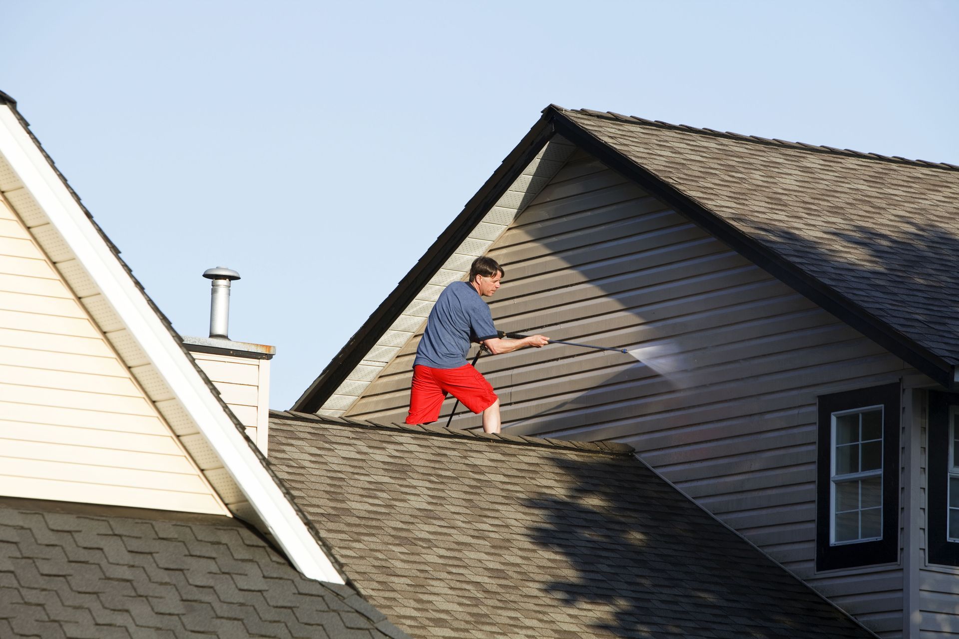 Person in red pants working on a roof beside a gray house.