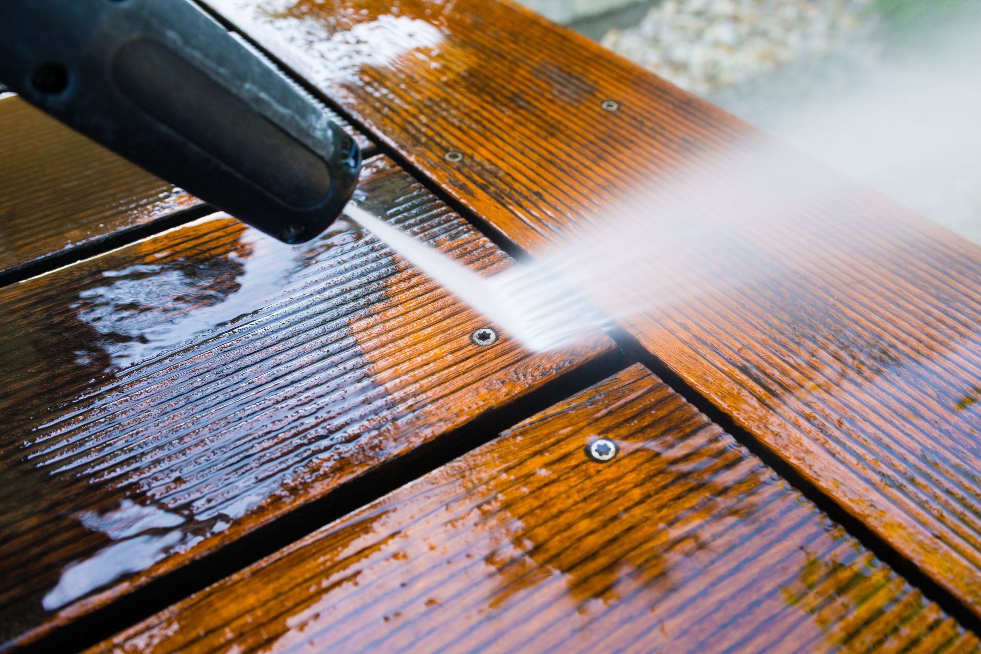 Pressure washer spraying water across a wet wooden deck, cleaning its orange-brown surface