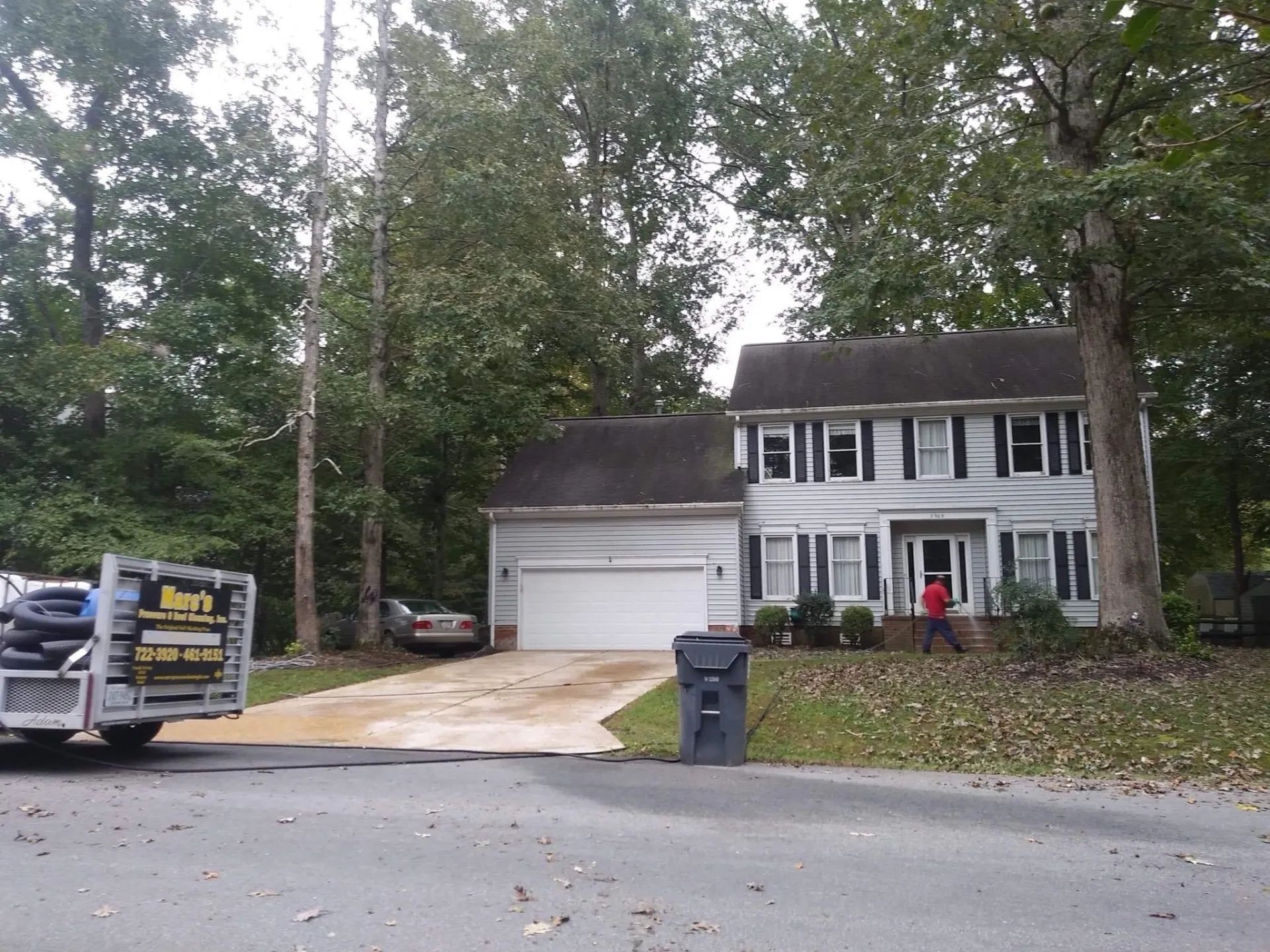 Two-story house with white trim, driveway, parked truck, trash bin, and tall trees along the street