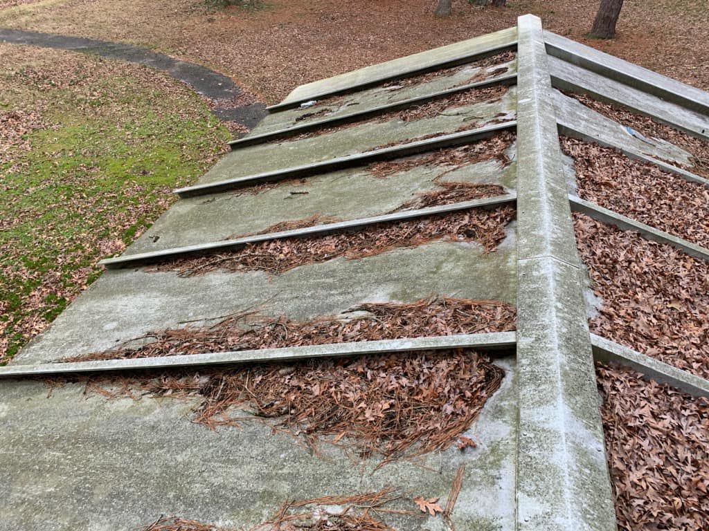 Weathered wooden ramp or bridge with white railings, covered in brown leaves in an outdoor setting