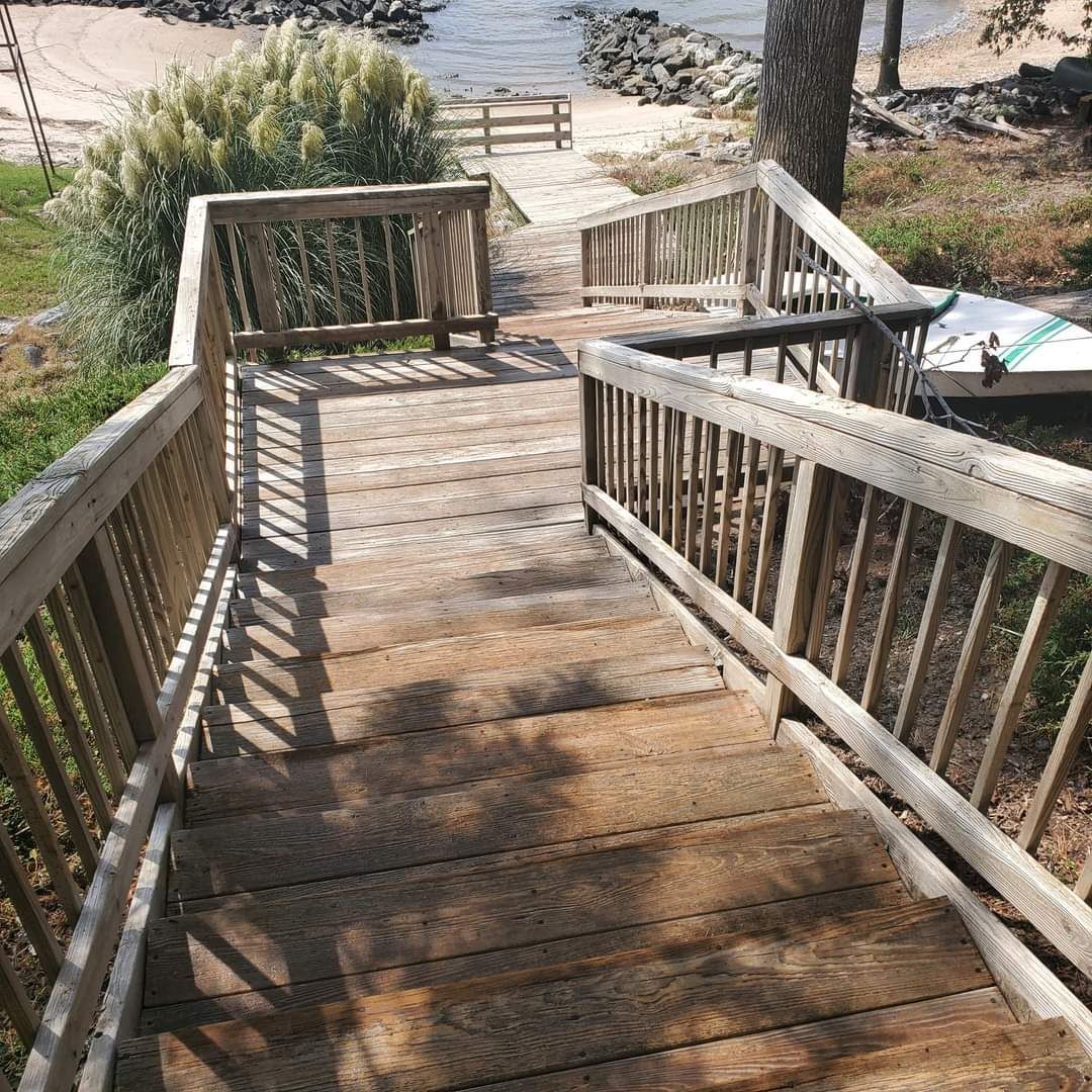 Wooden stairway and deck leading down to a sandy beach with a bench and railings, in bright sunlight