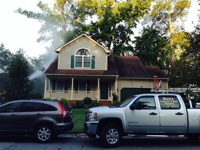 House with smoke near roof, parked cars in front, and trees behind