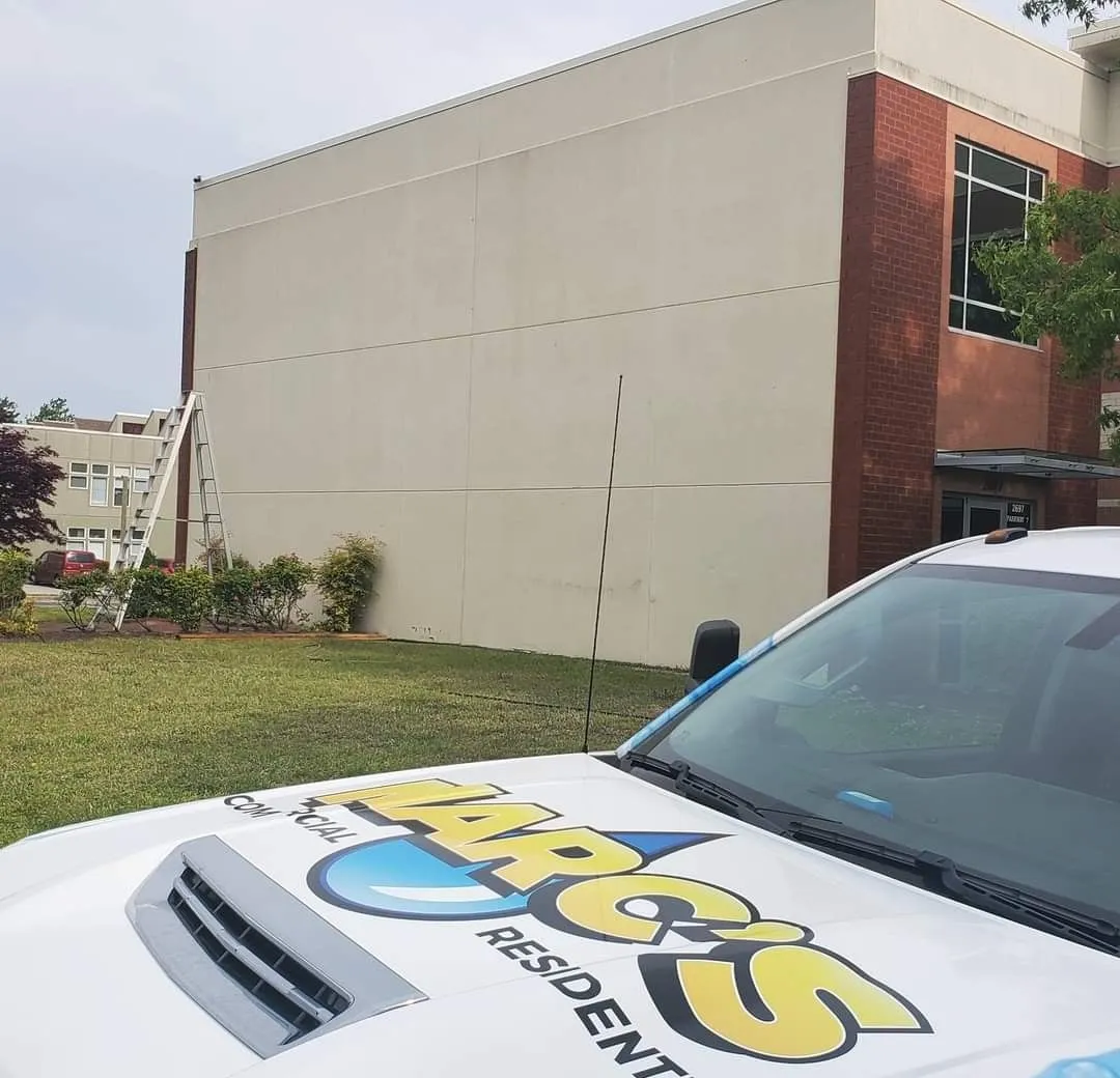White car hood with colorful logo in foreground beside a beige building and lawn
