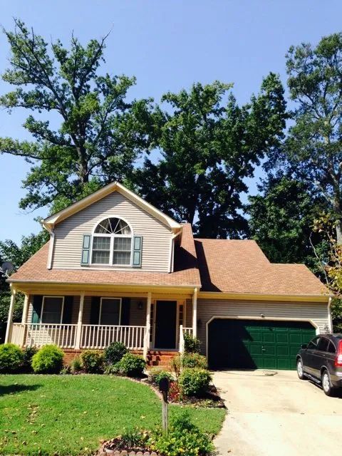 Two-story beige house with green garage door, front porch, and a car in the driveway under a clear sky