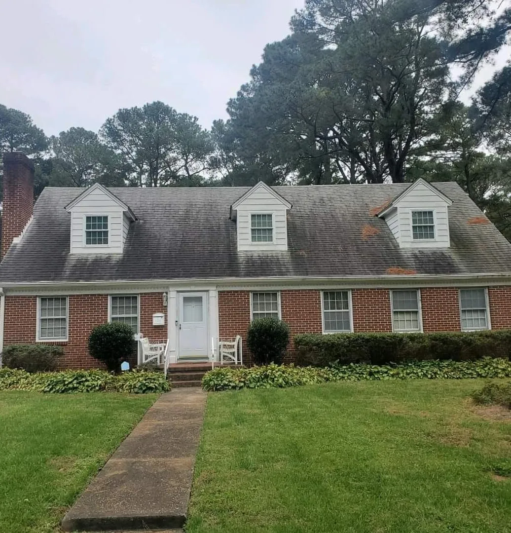 Brick house with white dormer windows, a front walkway, and a green lawn under cloudy trees