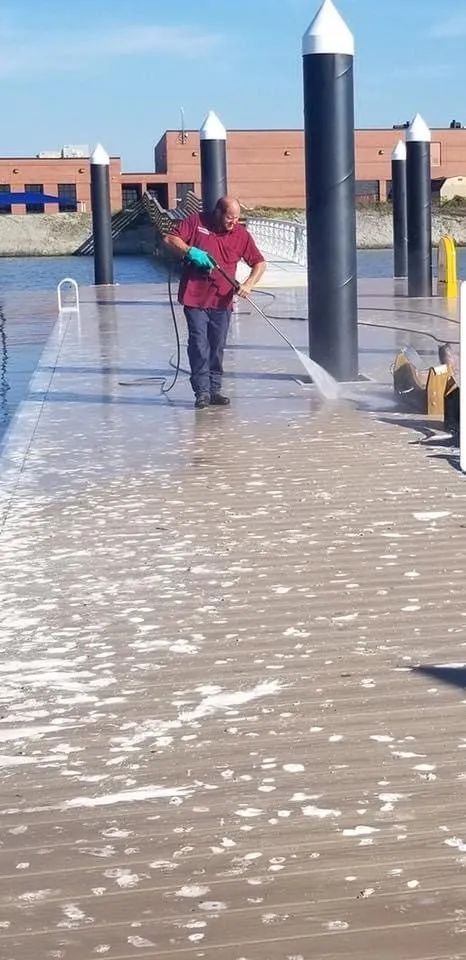 Person in red and teal jacket wading through flooded waterfront walkway beside dock posts and buildings