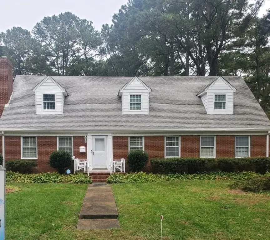 Brick ranch house with white dormers, front lawn, and central walkway under overcast skies