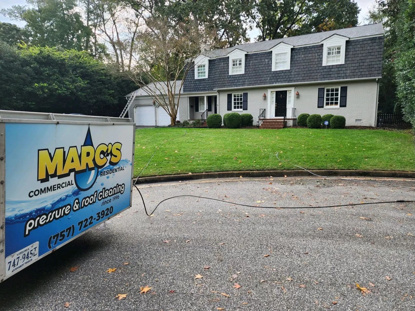 MARCOS Commercial Roofing sign in front of a white house with a dark roof and green lawn