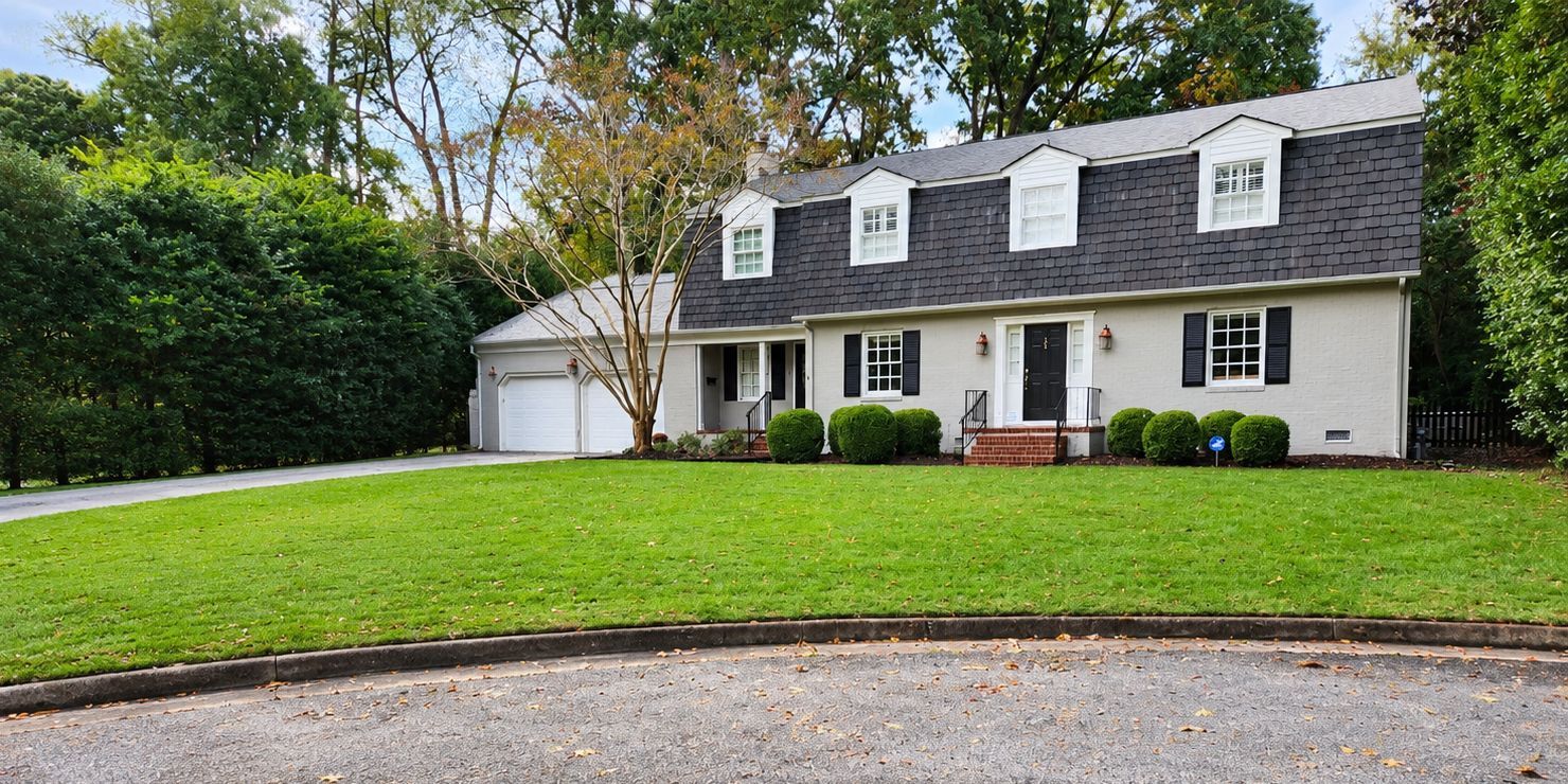 MARCOS Commercial Roofing sign in front of a white house with a dark roof and green lawn