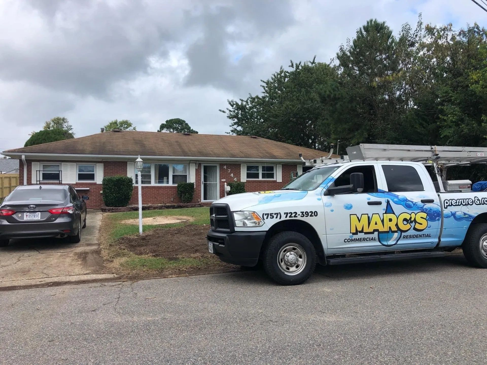 Marked utility truck parked in front of a brick house with a black sedan and cloudy sky