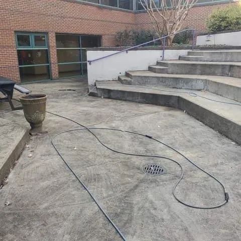 Brick courtyard with curved concrete steps, a drainage grate, and a black cable lying across the ground