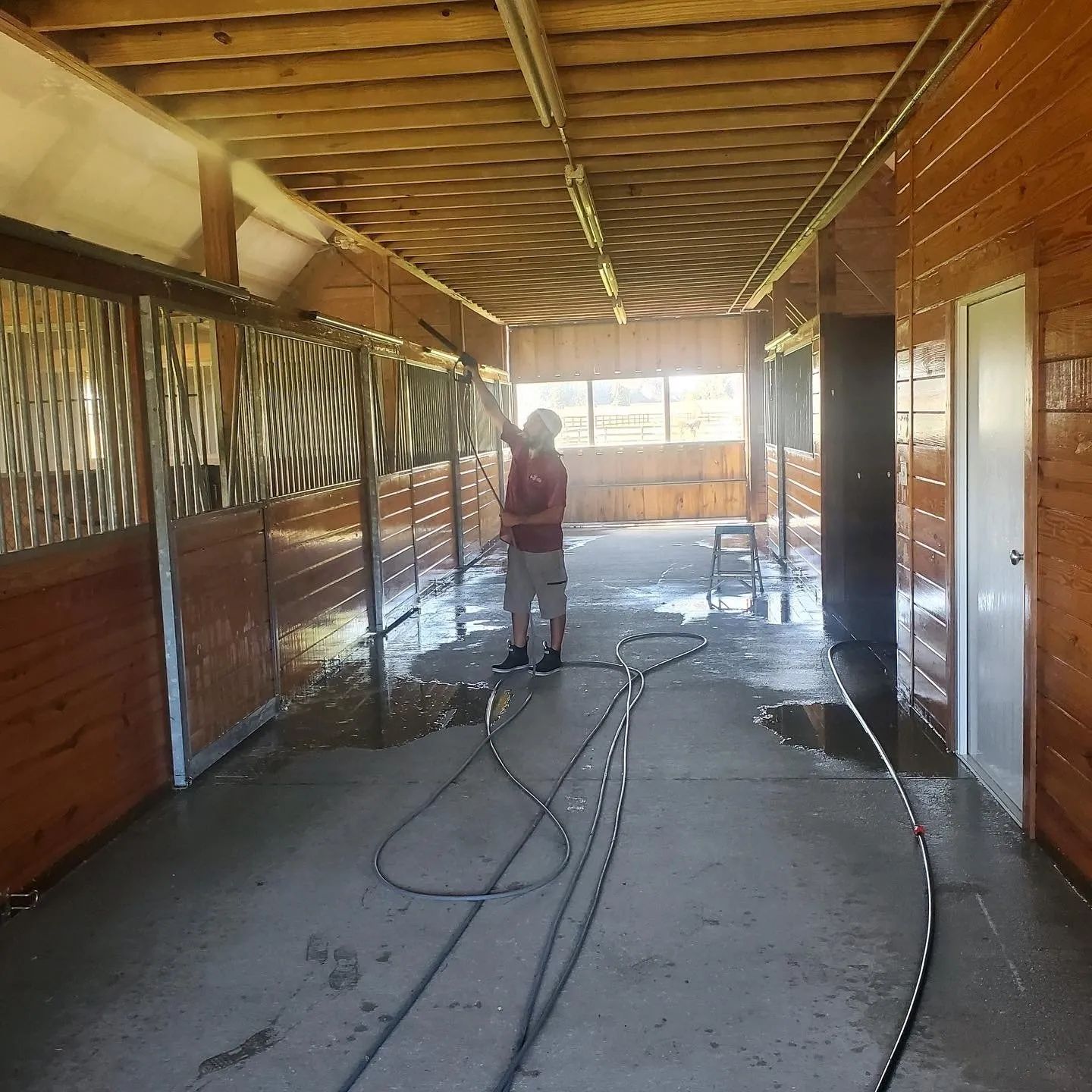 Person cleaning a covered porch with a pressure washer, hoses across the wet concrete floor.
