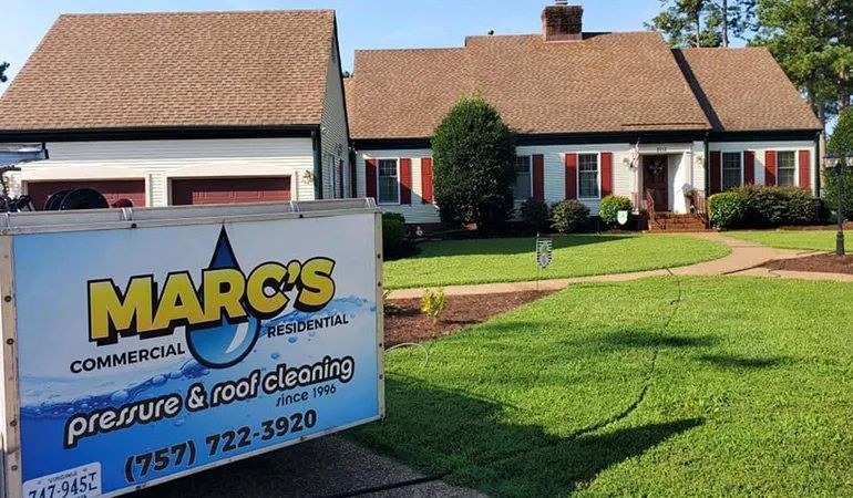 Marc’s Commercial pressure washing sign in front of a suburban house with a red roof and green lawn