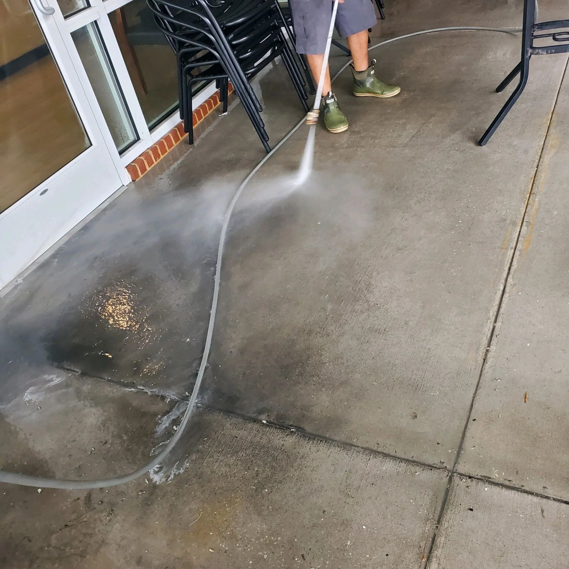 Person pressure-washing a wet concrete patio near a building entrance