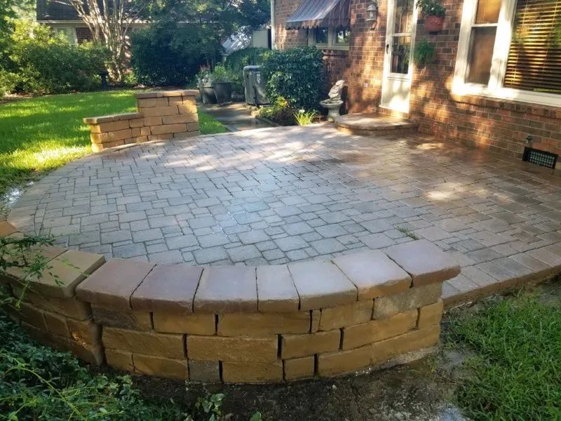 Brick-paved backyard patio with curved retaining wall and surrounding greenery