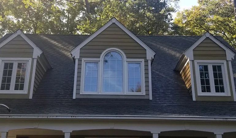 Gray house dormer with three windows, centered arched window and two side windows under trees