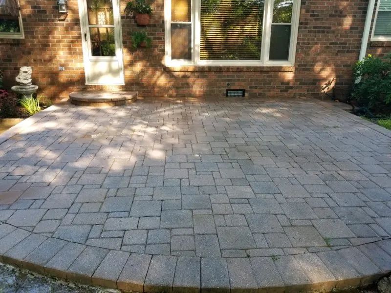 Brick patio with curved edge in front of a house, partly shaded by trees