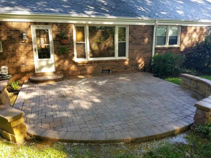 Brick patio with curved stone steps in front of a house's back door and windows