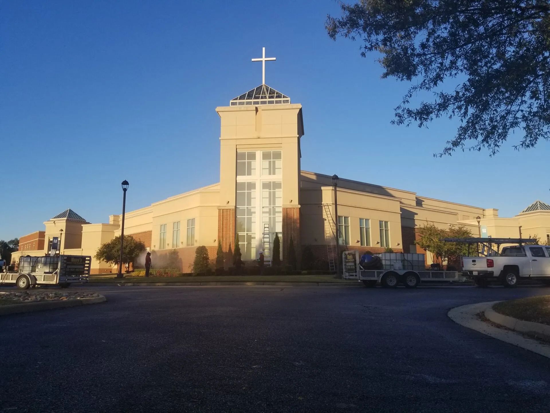 Large beige church building with a cross on top, viewed from a parking lot at sunset