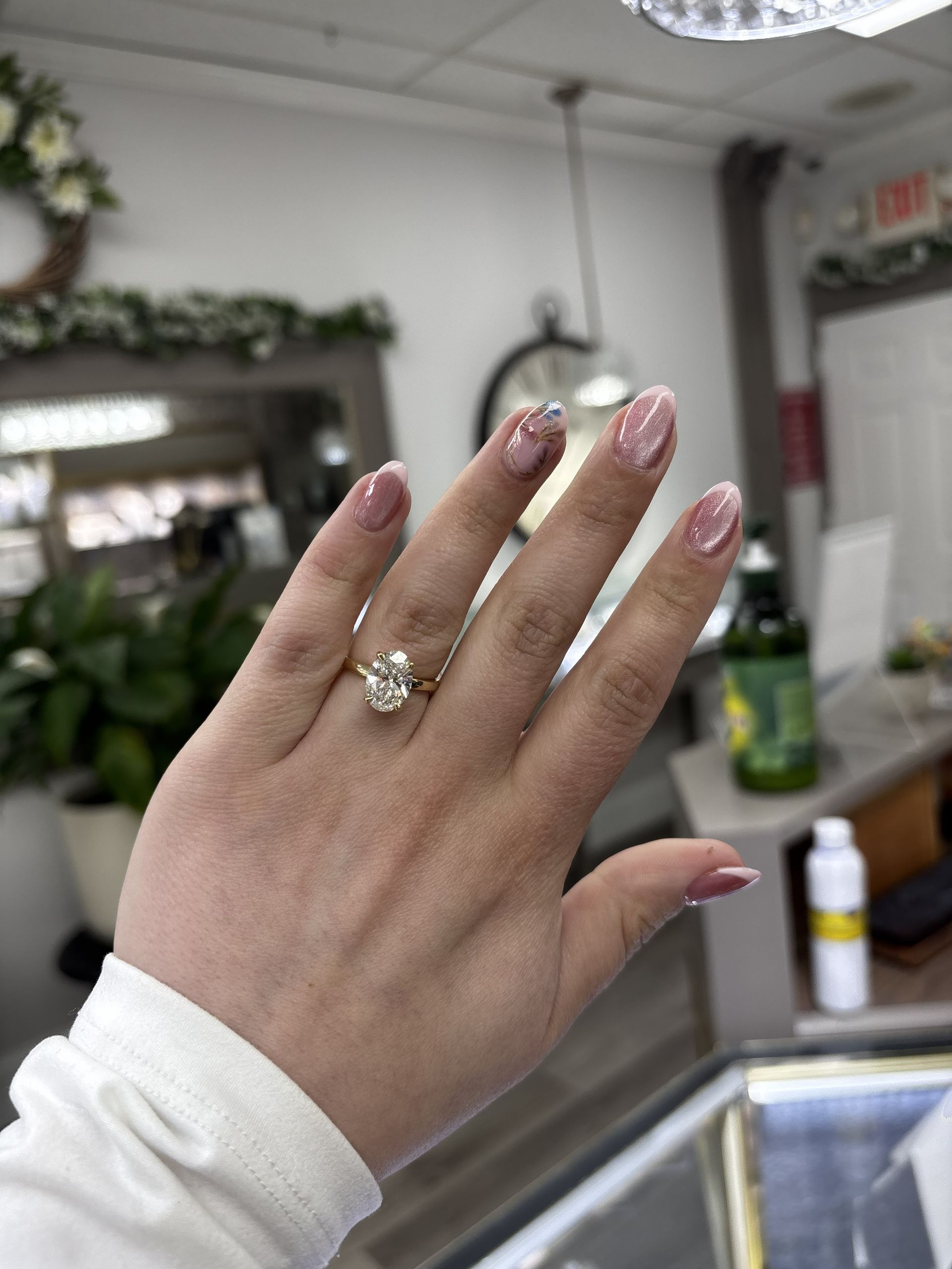 Hand with pink glitter nails and a ring held up in a salon, with a mirror and counter in the background