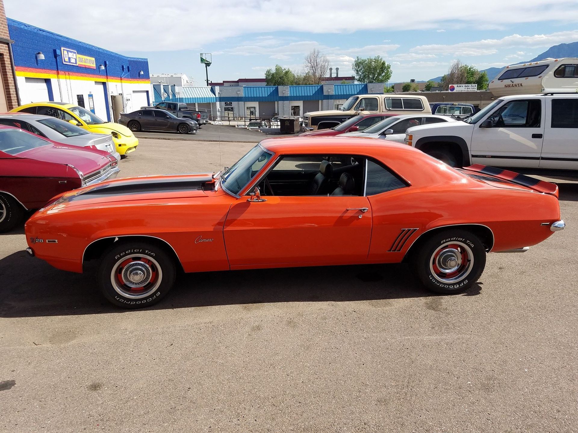 Orange vintage Camaro with black stripes, parked outside a building.