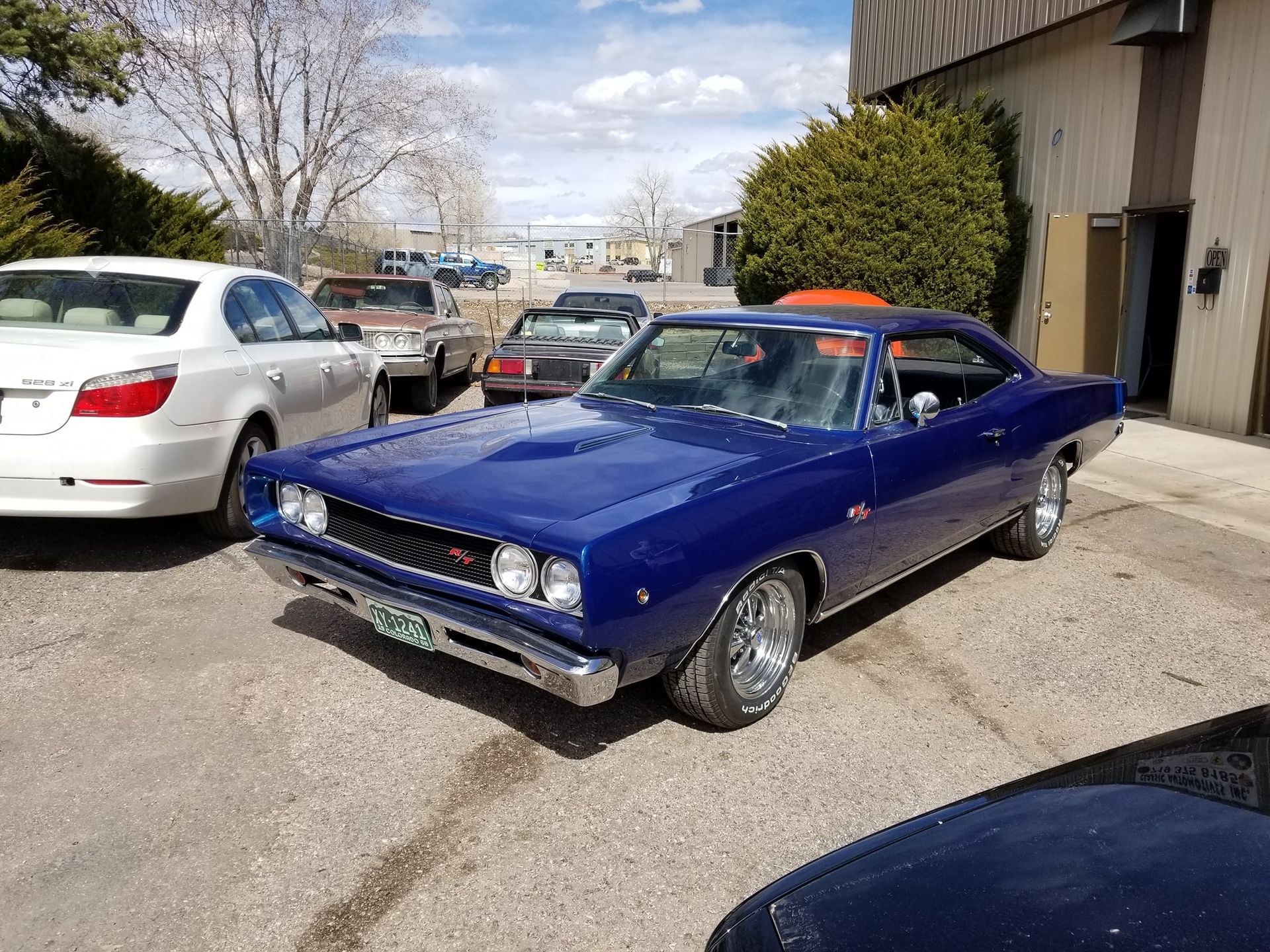 Blue classic car parked outside, with other vehicles and a building in the background.