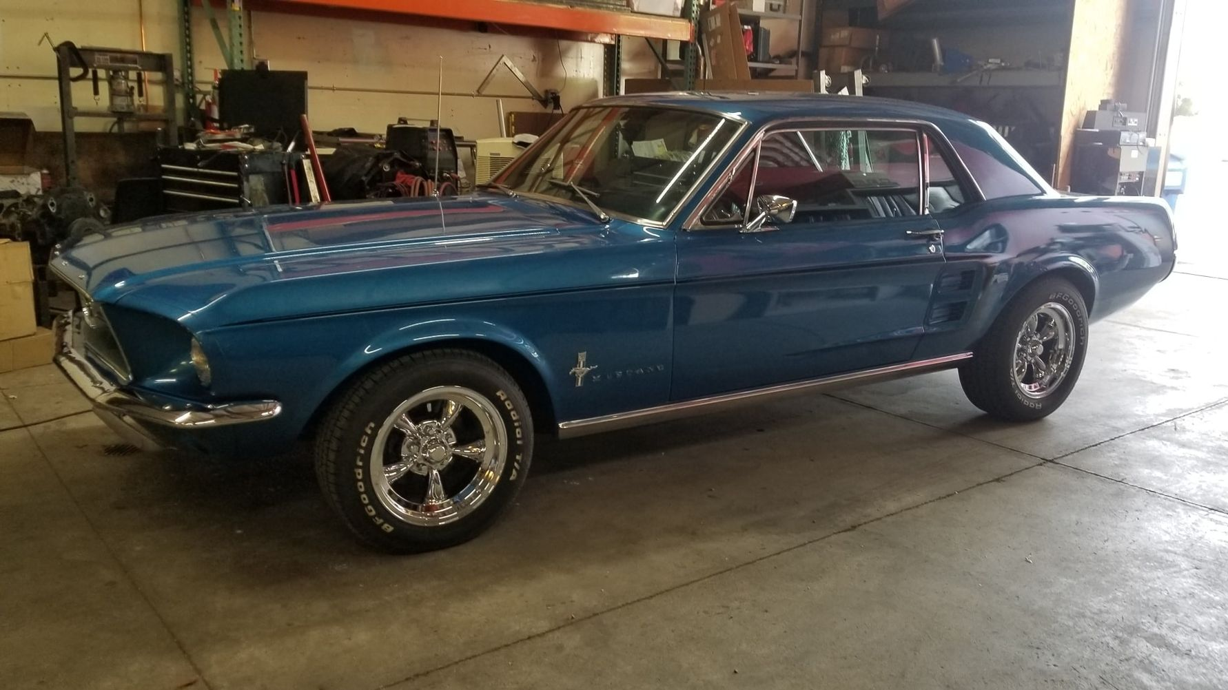 Blue classic Ford Mustang coupe parked in a garage. Chrome wheels, silver trim, and dark interior.