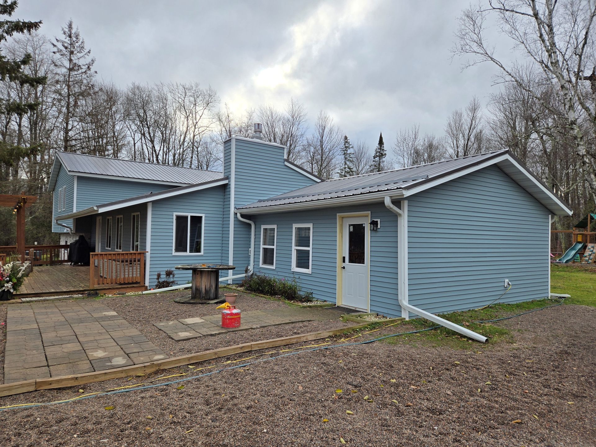 A blue house with white siding and a white door is sitting on top of a dirt field.
