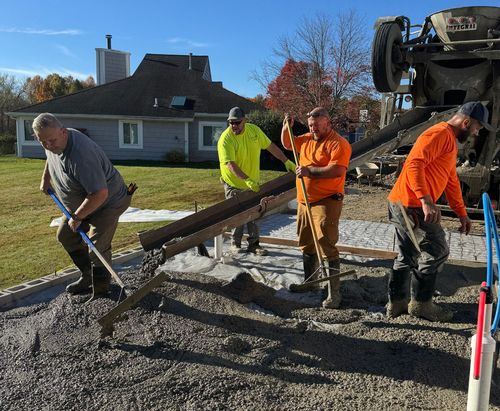 Workers pour wet concrete at a residential construction site with a concrete truck in the background