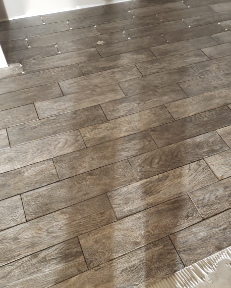 Wood-patterned dark laminate floor with sunlight and a small white rug edge in the lower right.
