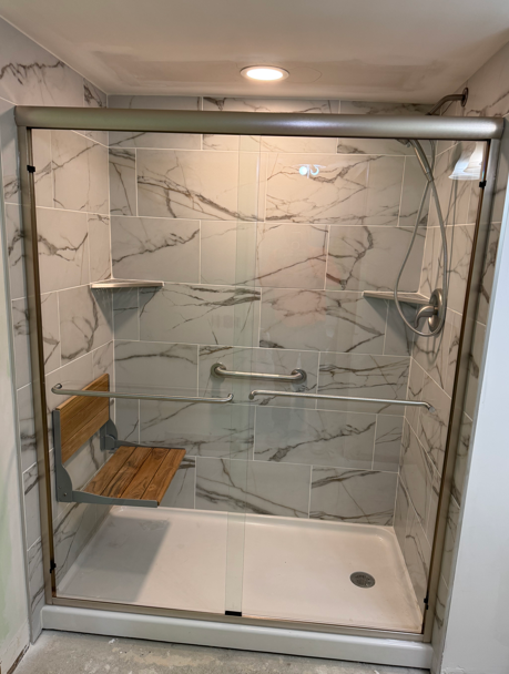 Glass-enclosed walk-in shower with marble-look tile, grab bars, and built-in bench seat
