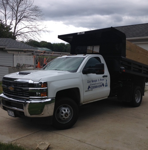 White dump truck parked in a driveway under cloudy skies, with a raised black dump bed.