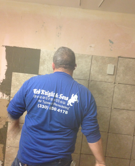 Worker in blue shirt painting a bathroom wall beside beige tile and pink plaster.