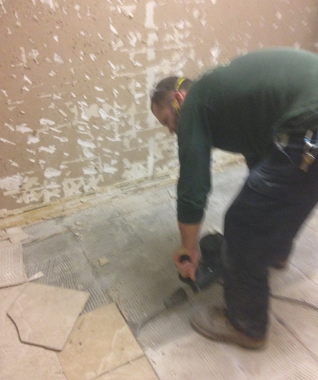 Worker kneeling to cut and fit floor tiles in a room with unfinished walls