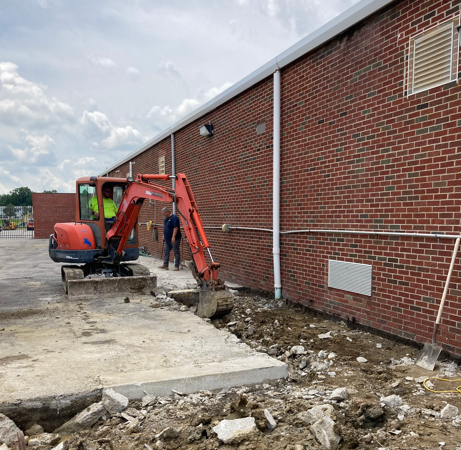 Orange excavator digging a trench beside a red brick building at a construction site