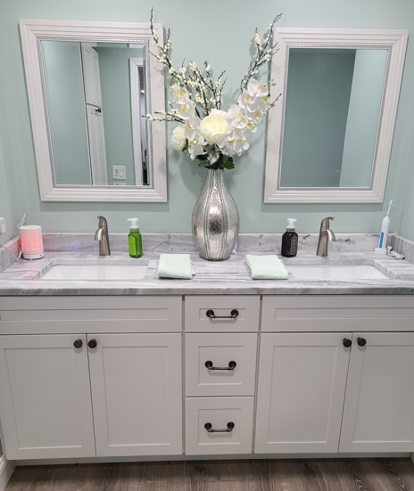 Modern double bathroom vanity with marble top, silver vase of white flowers, and matching mirrors on pale blue walls