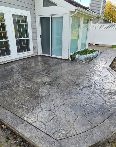 Concrete patio beside white house with glass doors and a raised garden bed