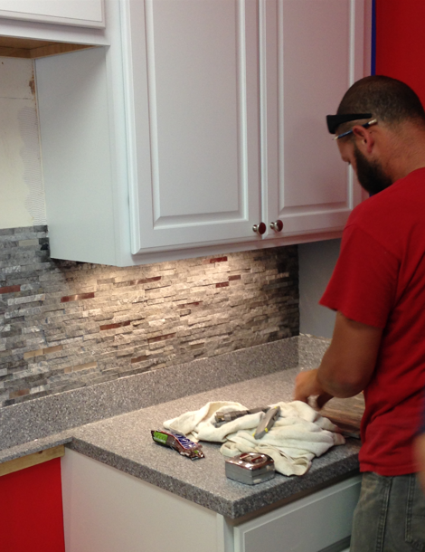 Person in red shirt working at a kitchen counter with a cloth and supplies under white cabinets