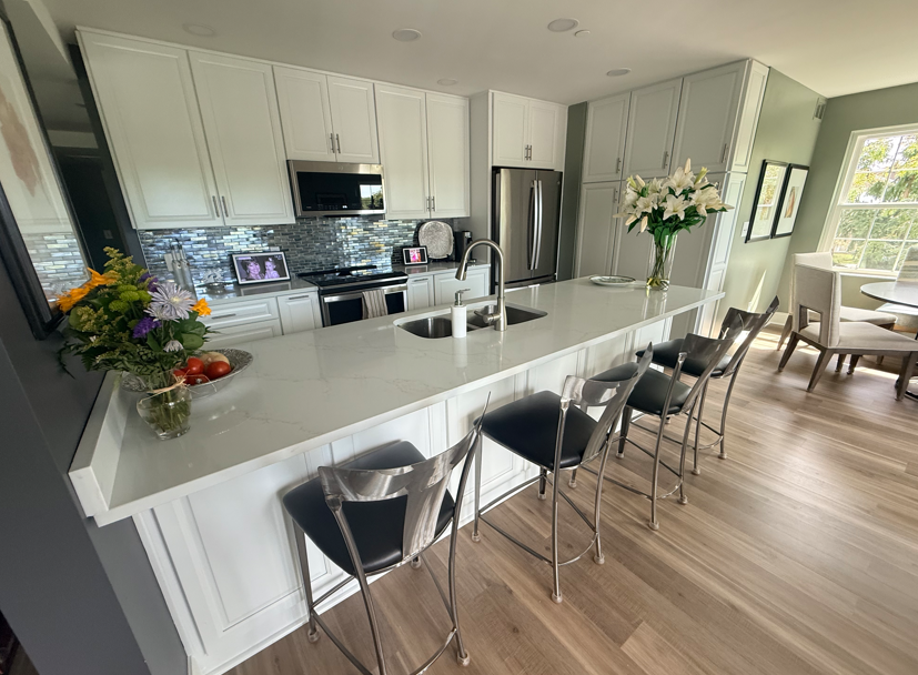 Bright modern kitchen with white cabinets, large island, bar stools, and dining area by a window.