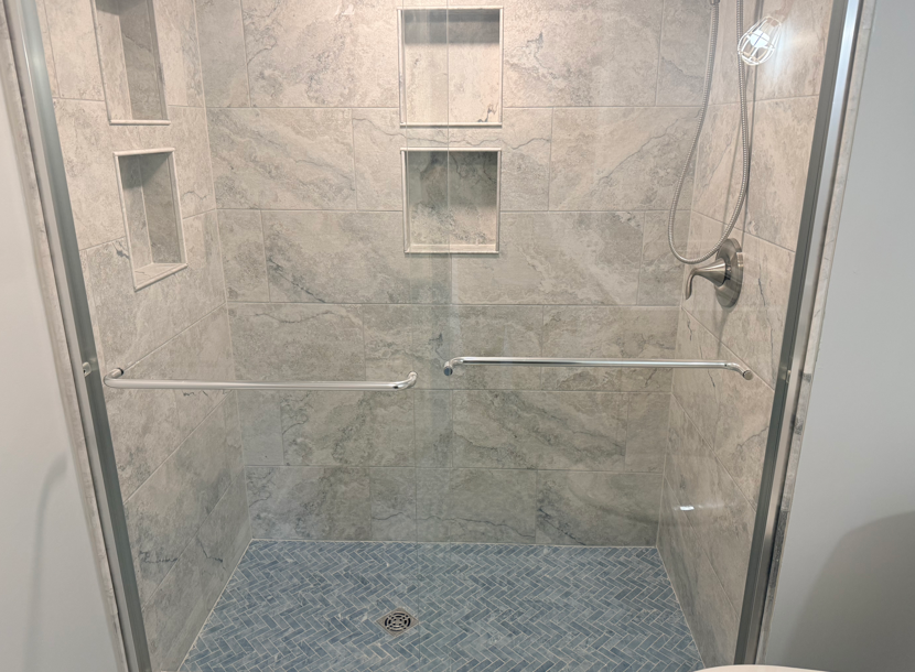 Glass shower enclosure with marble walls, built-in shelves, and a blue tiled floor