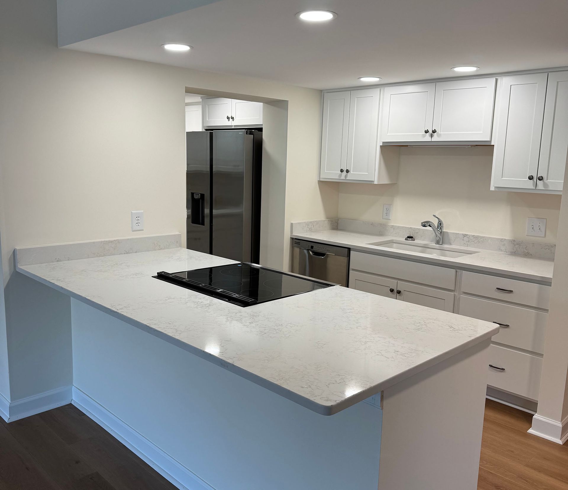 Bright modern kitchen with white cabinets, gray island, stainless fridge, and hardwood floors