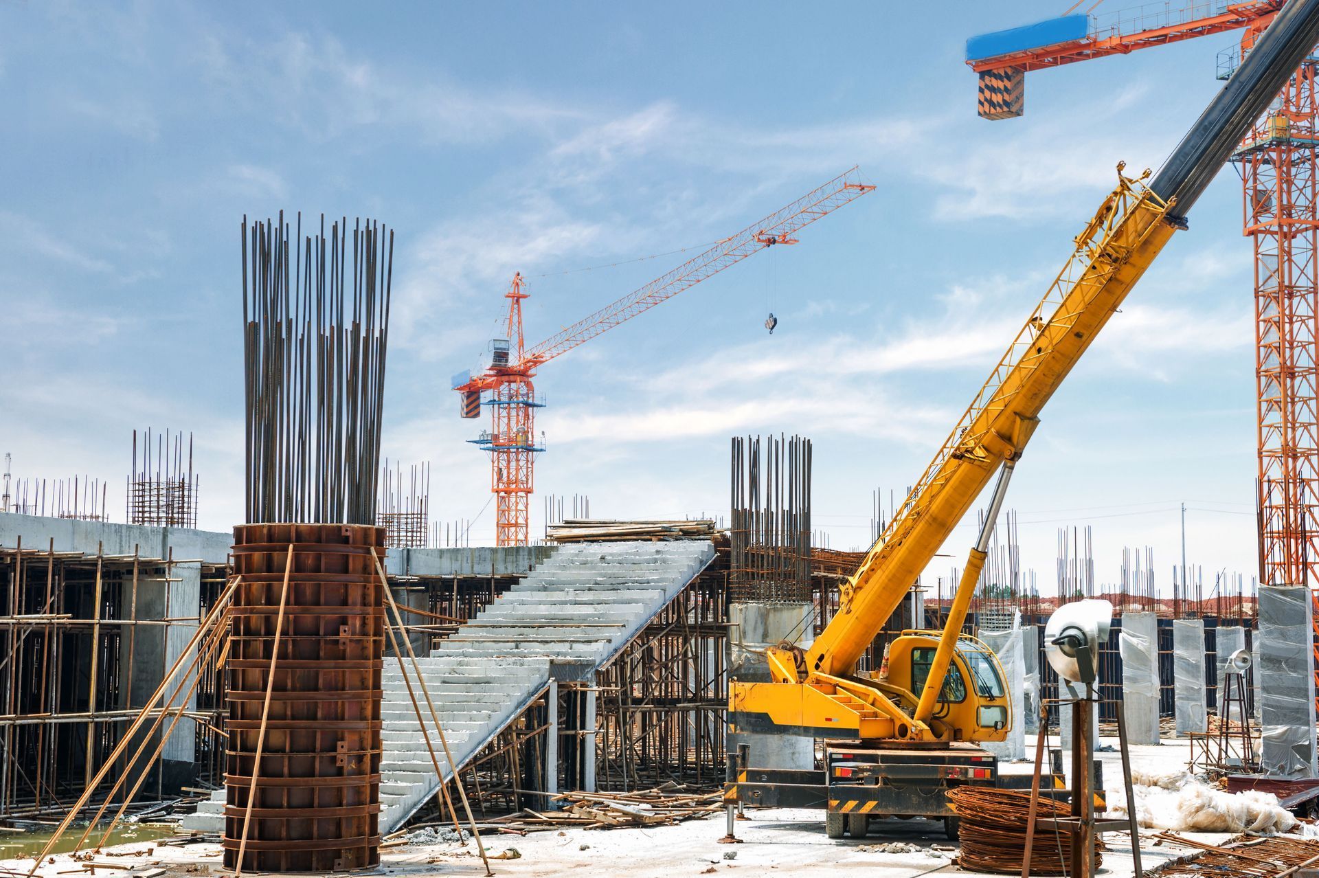 Construction site with crane, scaffolding, rebar, and workers under a blue sky