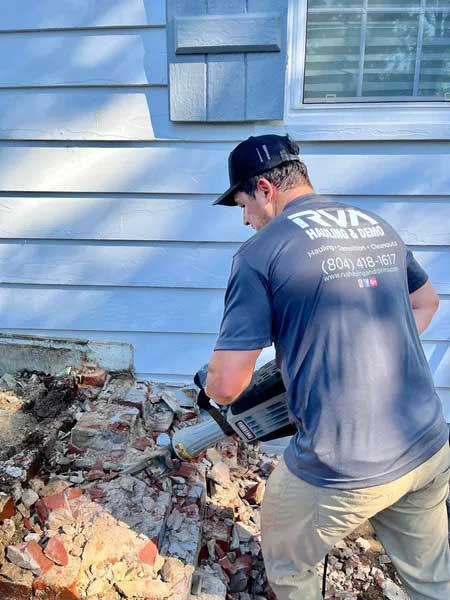 Worker removing debris beside a blue house exterior with a small window.