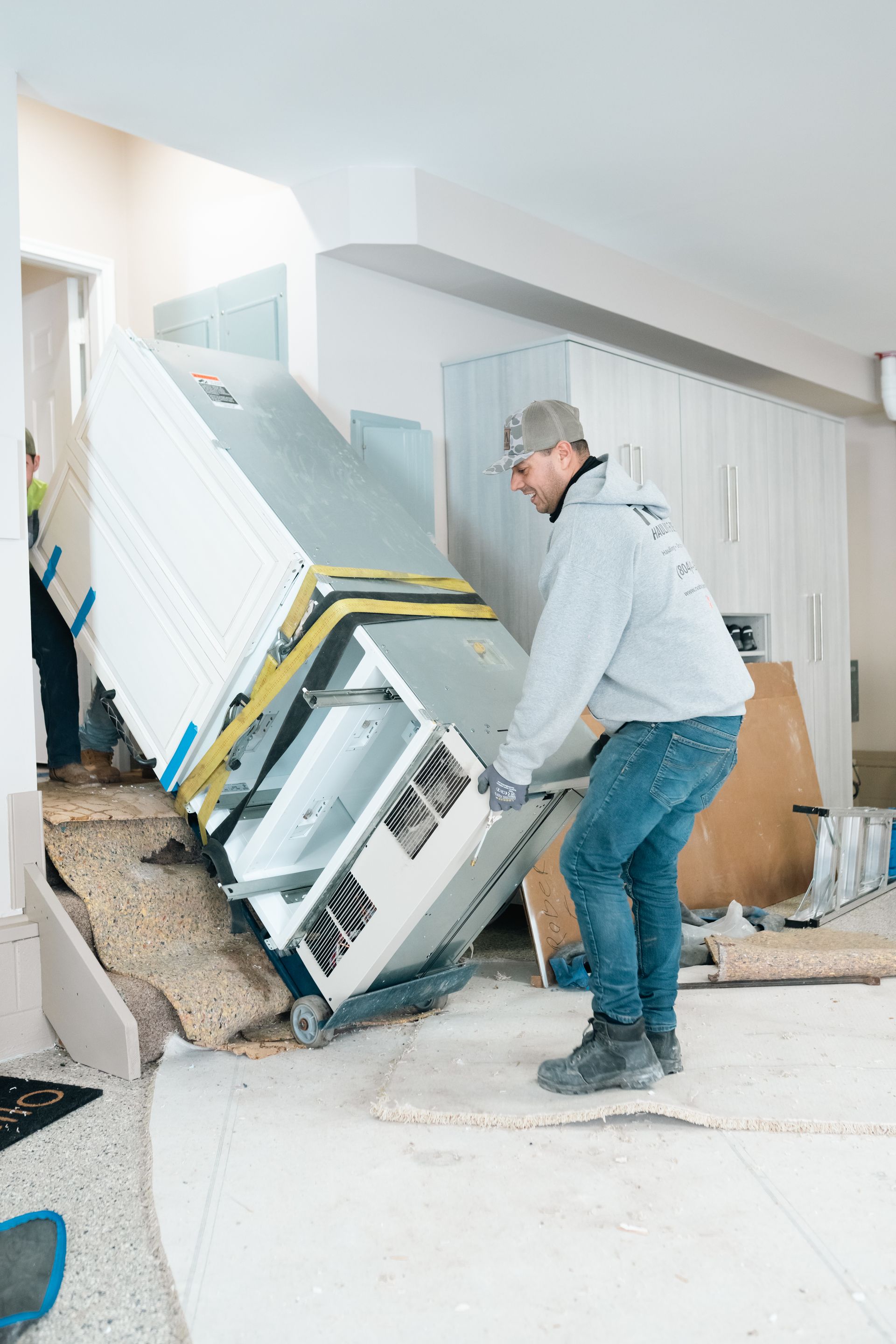 Man moving a toppled white cabinet in a damaged, cluttered room after flooding or collapse