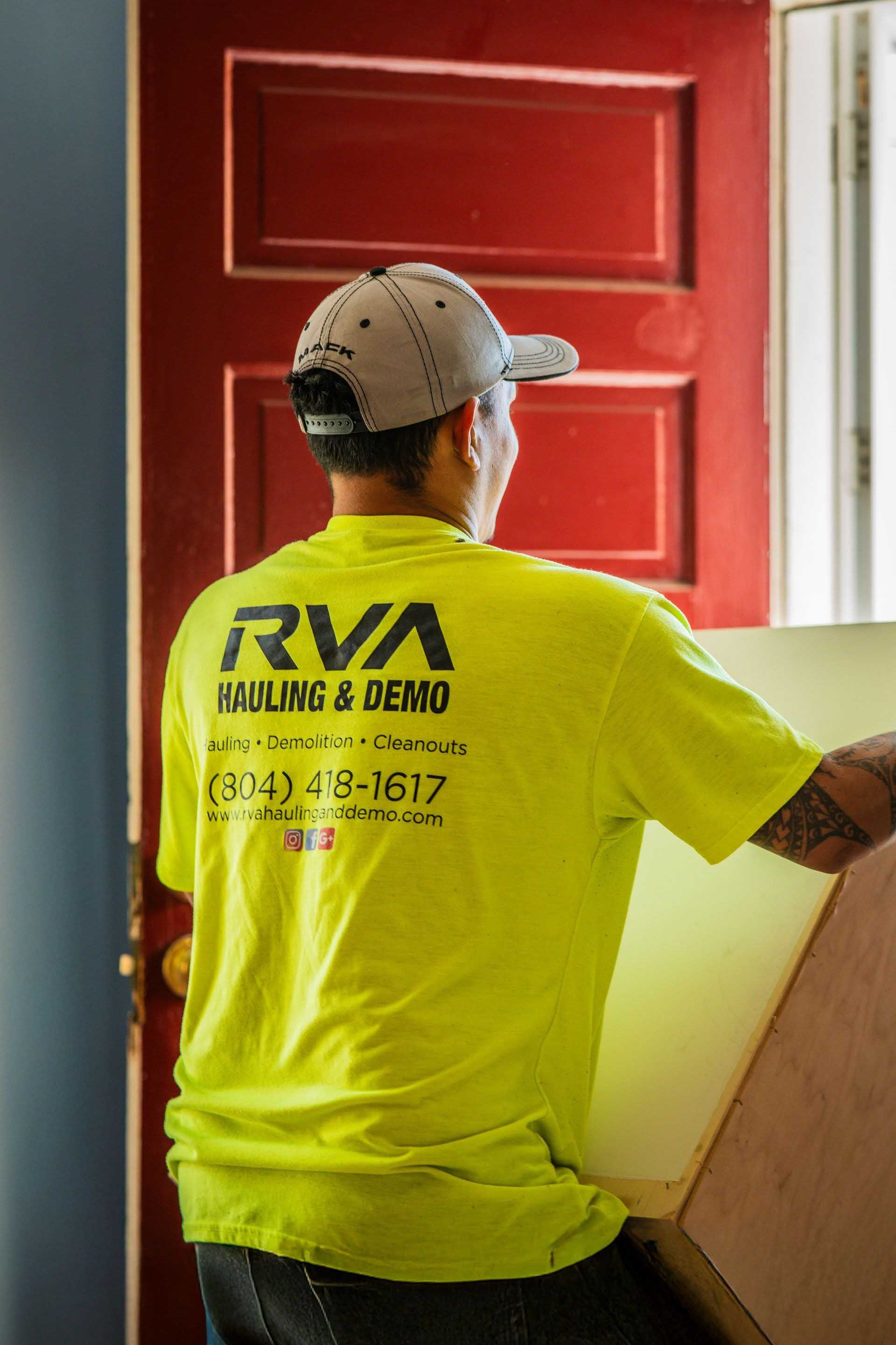Worker in neon yellow shirt carrying plywood inside a home with a red door.